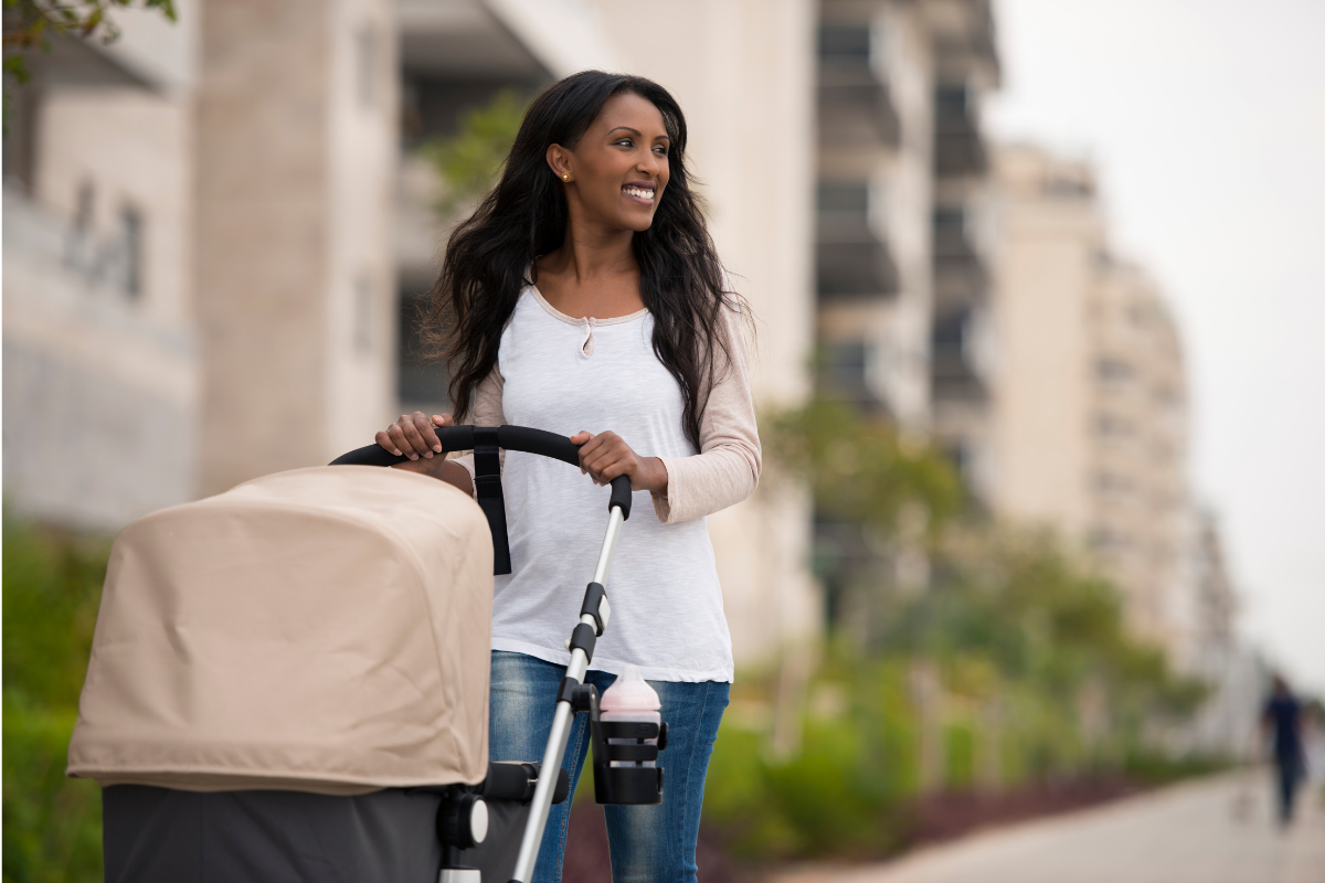 Black woman smiling while pushing a stroller down a city street