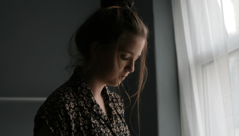 woman looking sad beside window (mothering with chronic illness, multiple sclerosis)