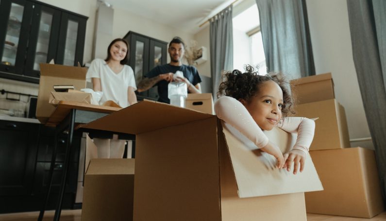 little girl playing inside a moving box, while parents look on (making a new house a home for kids)