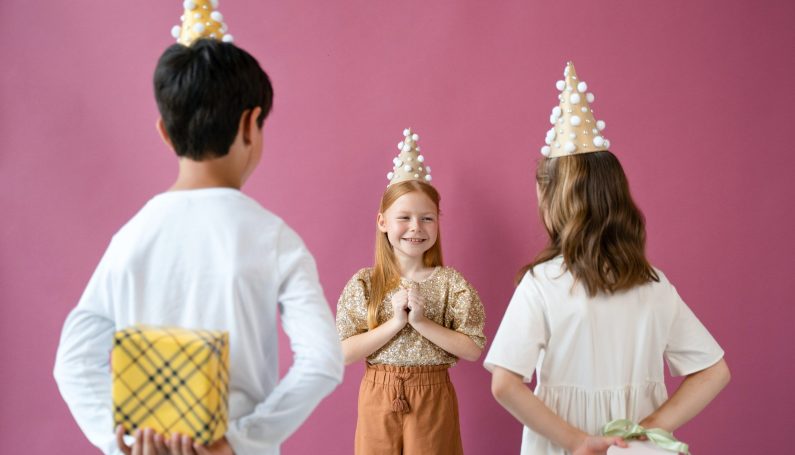 Girl with red hair in the center faces two children with gifts behind their backs
