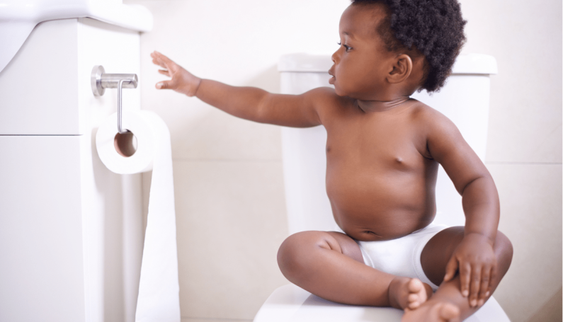 child sitting on closed toilet seat reaching for toilet paper (potty training and potty learning)