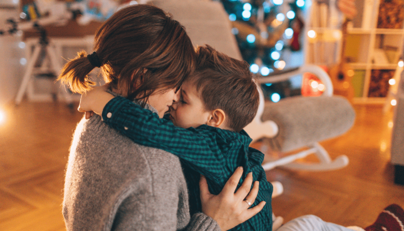 mom and child hugging near Christmas tree (single parent holiday traditions)