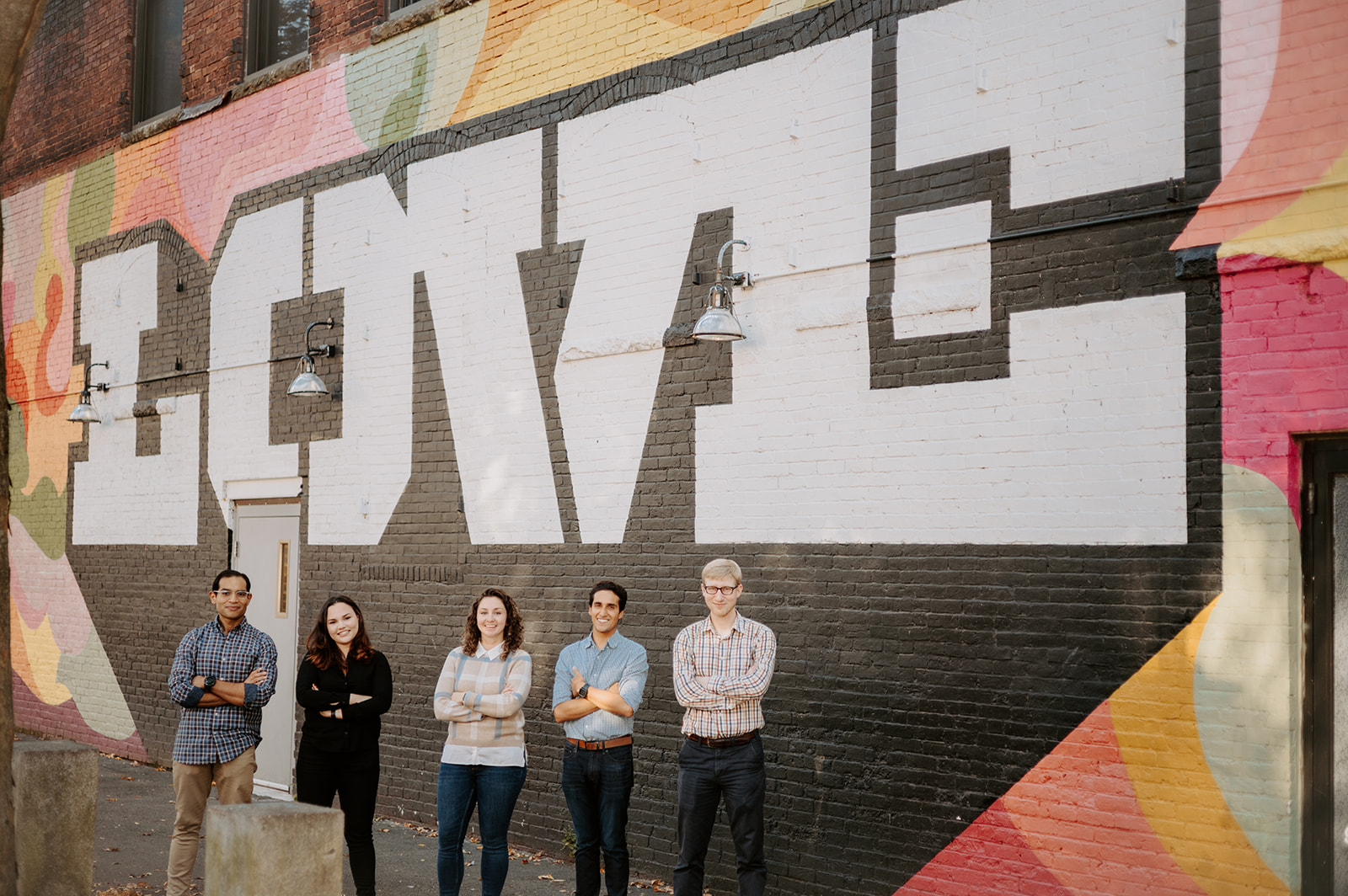 Photo of five adults standing in front of a mural that says "Love"