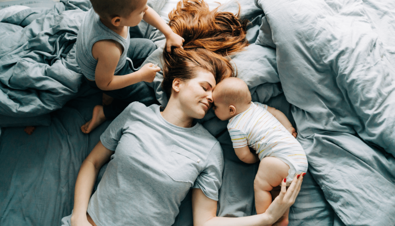stay-at-home mom on bed with two children surrounding her