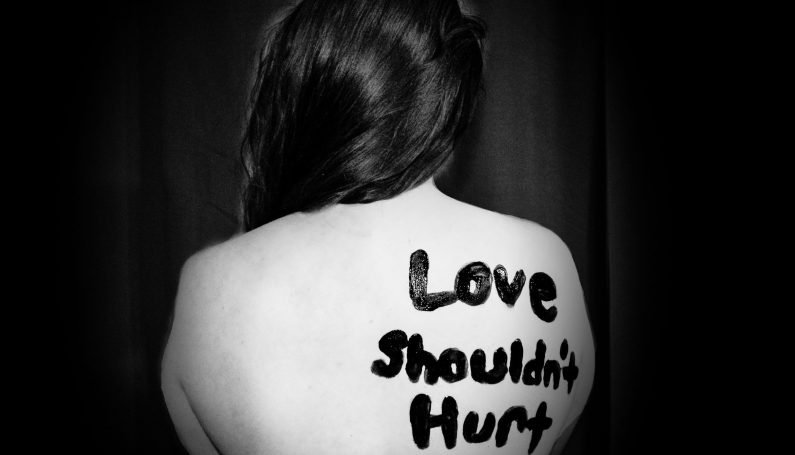 black and white photo of a woman with a bare back with the phrase "Love shouldn't hurt" painted on her skin