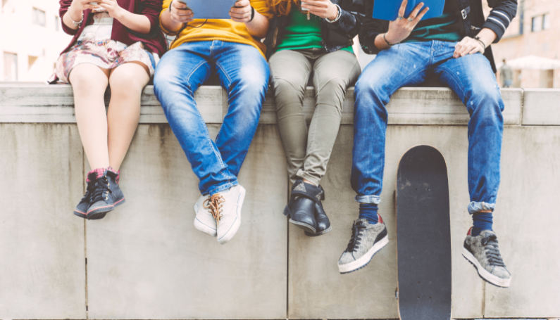 group of teenagers looking at their individual phones, tablets, devices, and books