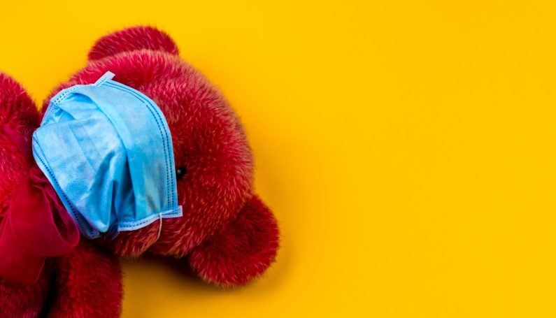 Yellow background with red stuffed animal bear wearing facemark