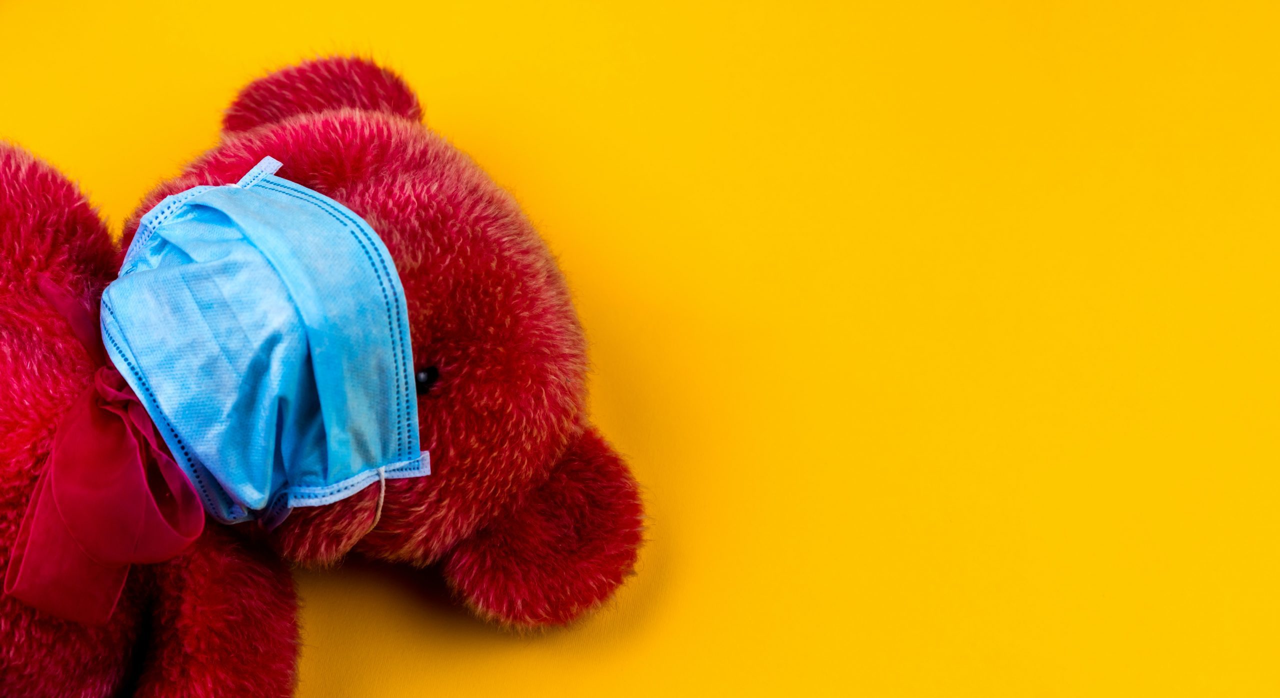 Yellow background with red stuffed animal bear wearing facemark